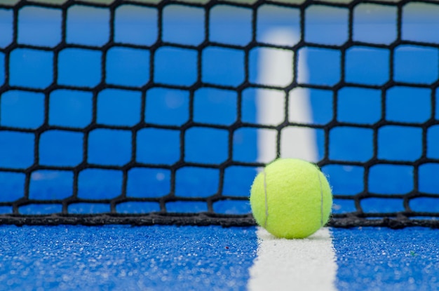 Selective focus, ball on a blue paddle tennis court on the line near the net