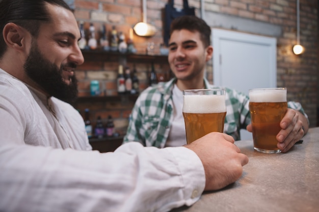 Selective focus on beer glasses in hands of male friends at the bar