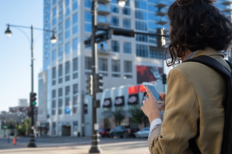 Selective focus of brunette woman on her back looking on smartphone for directions in a big city, with copy space