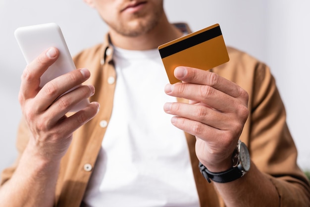 Selective focus of businessman holding credit card while using smartphone in office