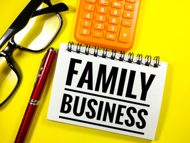 黄色の背景に家族経営のテキストを含む電卓眼鏡とペンの選択的な焦点