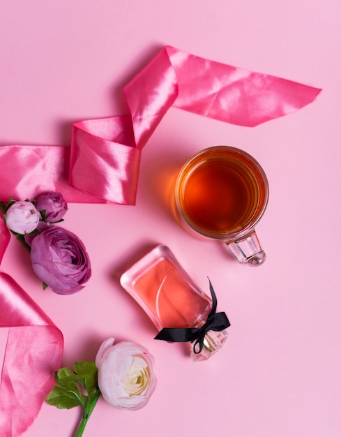 Selective focus: ceylon black tea in a transparent mug on a pink table with a pink satin ribbon. women's perfume and flowers.