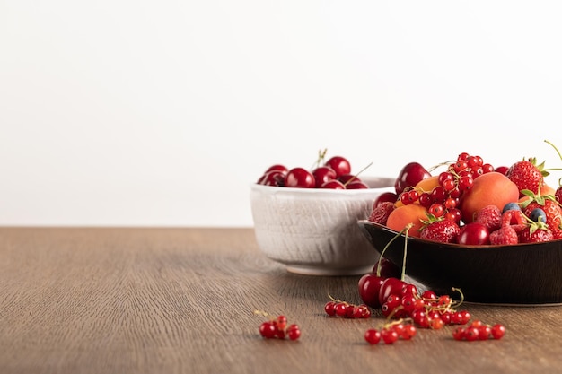 Selective focus of cherries in white bowl and mixed berries on plate on wooden table isolated on