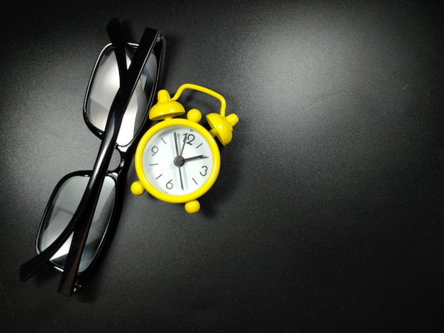 Selective focus of clock and glasses on black background with copy space