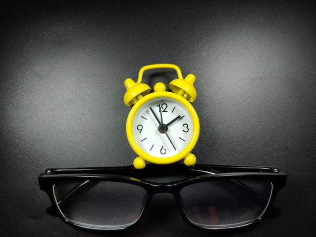 Selective focus of clock and glasses on black background with copy space