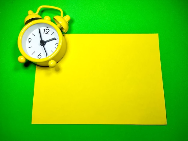 Selective focus of clock and note paper on green background with copy space