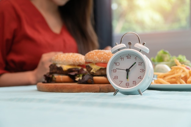 Photo selective focus of clock, young woman ready to eating breakfast