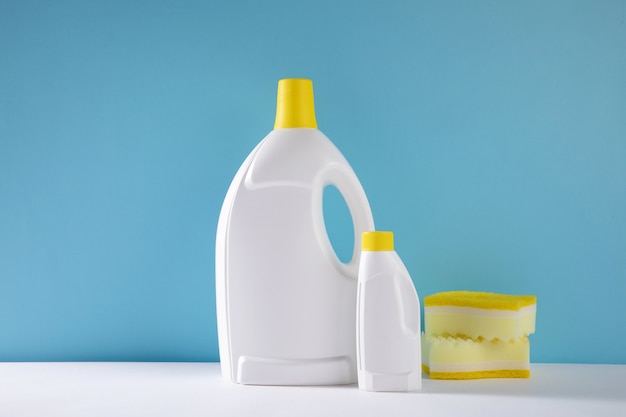 Selective focus closeup of gallons of cleaning detergent and sponges on a blue wall