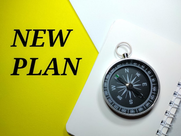 Selective focus compass on a notebook with word NEW PLAN on a white and yellow background