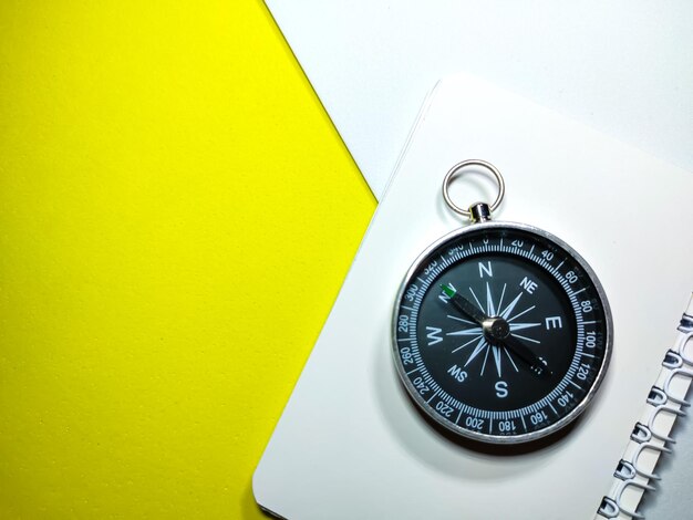 Selective focus of compass and notebook on yellow and white background with copy space