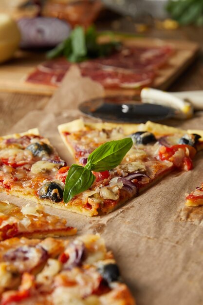 Foto messa a fuoco selettiva della pizza italiana tagliata con olive su carta da forno vicino agli ingredienti e coltello da pizza acceso