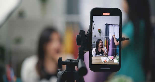 selective focus on display of smartphone while young vlogger woman influencer live streaming review and sale new fashion clothes at home studio small business and influencer on social media concept
