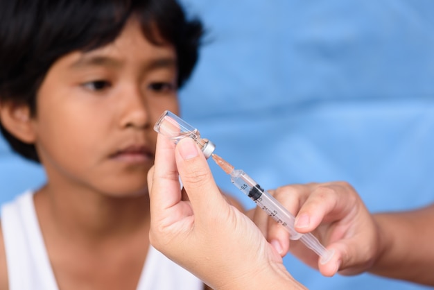 Selective focus doctor hand holding syringe and vial for vaccine with blurry Asian girl ba