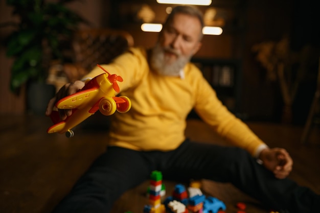 Selective focus of elderly man in trendy fashion outfit playing toy airplane