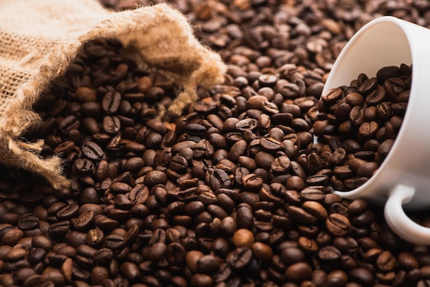 Selective focus of fresh roasted coffee beans and white cup near sack