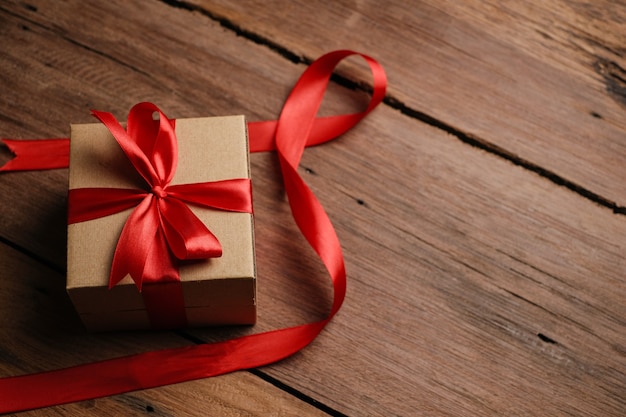 Selective focus of gift box with red ribbon and love shaped paper over rustic wooden table, top view flat lay.