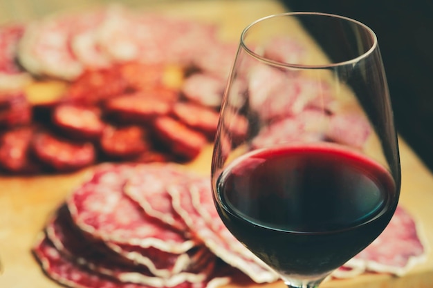 Selective focus on glass of red wine with traditional salami sliced on cutting board