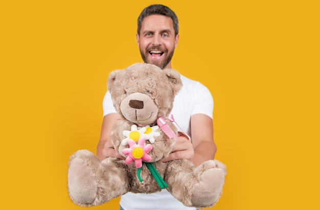남자의 선택적 초점은 노란색 배경에 고립 된 발렌타인 데이 장난감 곰을 잡아