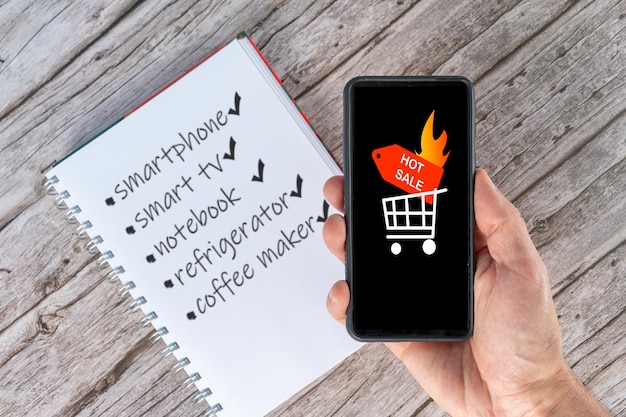 Foto messa a fuoco selettiva di una mano che tiene uno smartphone che annuncia la vendita calda e una lista dei desideri