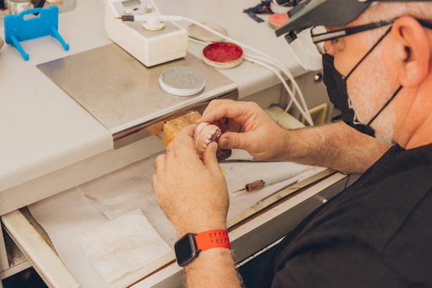 Selective focus on the hands of a caucasian adult male sitting at a workshop table working with a dental mould in a dental laboratory specialising in dental bone ceramics to create porcelain crowns.