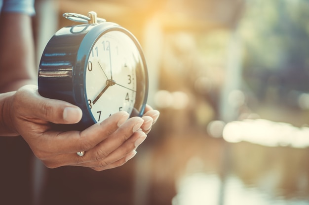 Selective focus of hands holding of alarm clock with nature background.