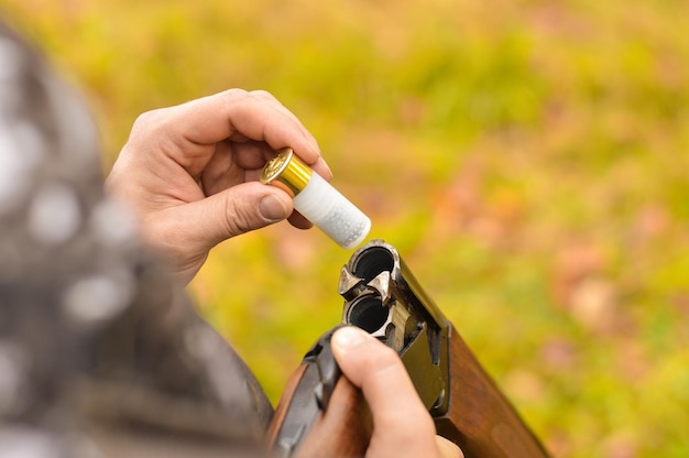 Selective focus of the hands of a man in a camouflage protective suit who loads a doublebarreled shotgun The concept of hunting