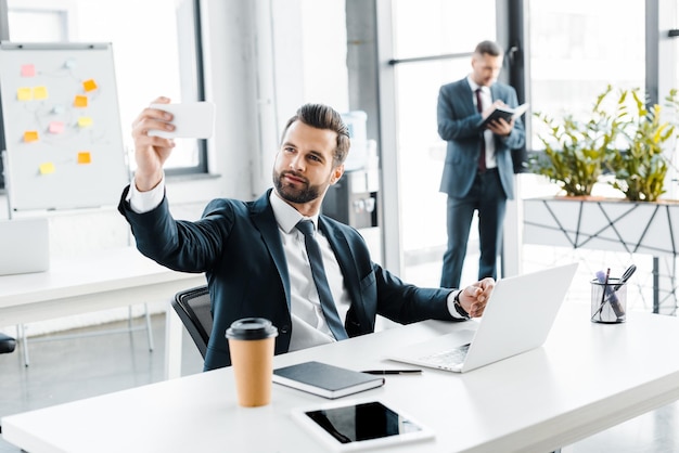 Selective focus of happy businessman taking selfie in modern office