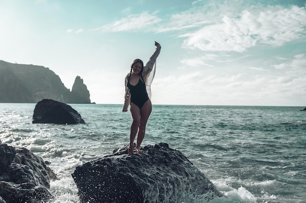 Избирательный фокус Счастливая беззаботная чувственная женщина с длинными волосами в черных купальниках позирует на закатном пляже Силуэт молодой красивой игривой позитивной женщины на открытом воздухе Летние каникулы и концепция поездки