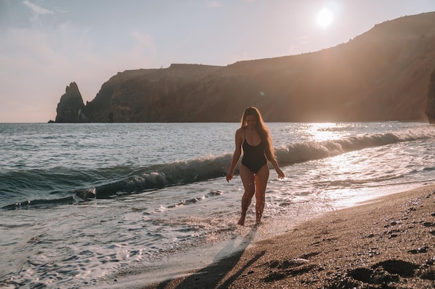 Selective focus happy carefree sensual woman with long hair in black swimwear posing at sunset beach