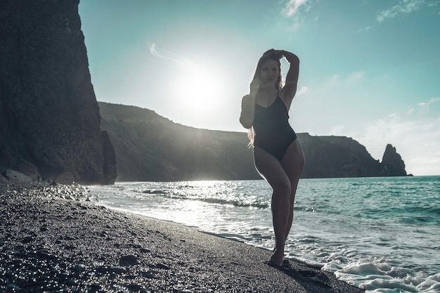 Selective focus happy carefree sensual woman with long hair in black swimwear posing at sunset beach