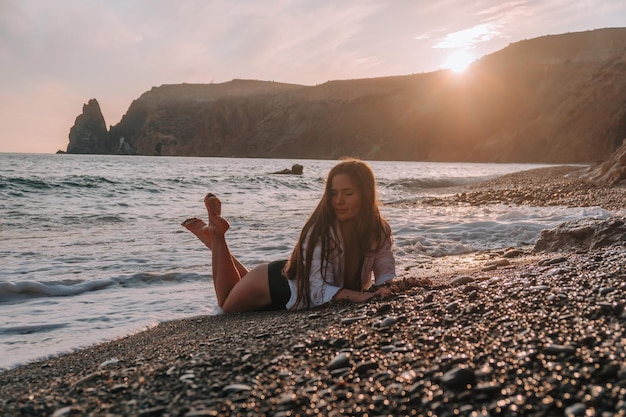 Donna sensuale spensierata felice del fuoco selettivo con i capelli lunghi in costume da bagno nero che posa alla spiaggia del tramonto