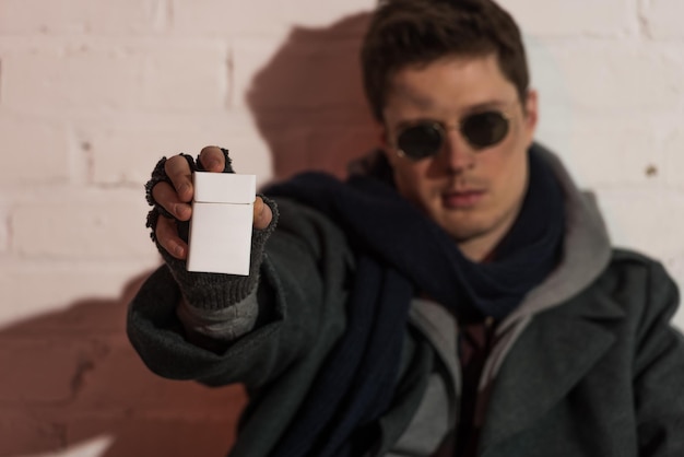 Selective focus of homeless man in fingerless gloves and dark glasses holding cigarette pack in