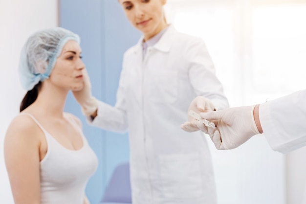 Selective focus if a medical tool being given to a professional female plastic surgeon during the operation