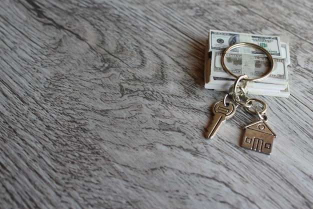 Selective focus image of house shaped keychain and stack of money Home ownership real estate concept