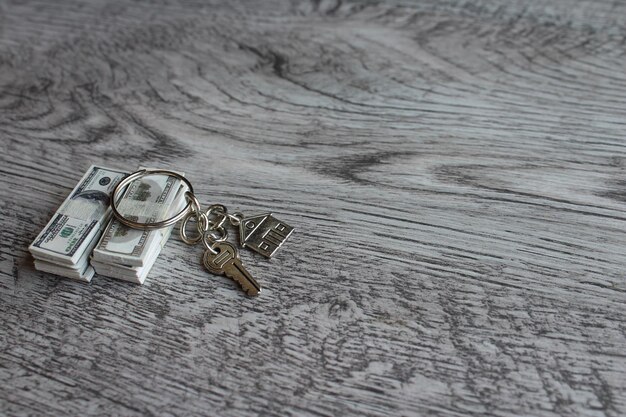 Selective focus image of house shaped keychain and stack of money Home ownership and real estate concept