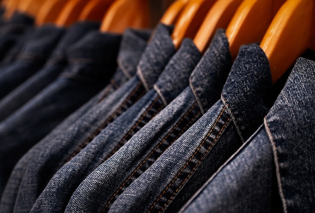 Selective focus on jacket jeans hanging on rack in clothes shop. Denim jeans with jeans pattern.