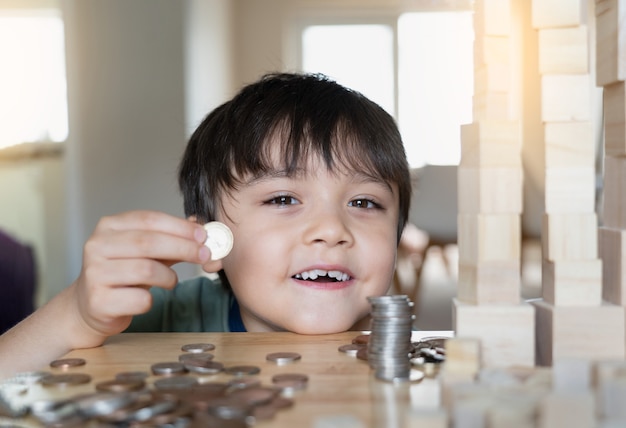 Selective focus kid holding money coin on his hand with smiling\
face with blurry foreground of coin on table.