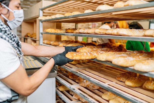 Selective focus of Latino baker shelving freshly baked bread with a protective face mask