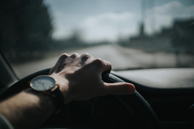 Selective focus of a male hand with a wristwatch holding the steering wheel of a car