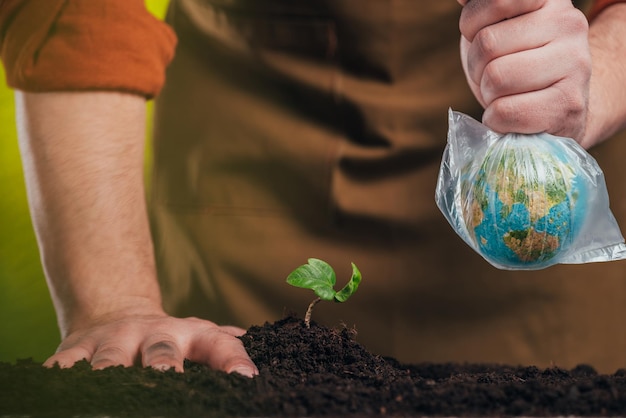 Selective focus of man planting young plant and holding globe model in plastic bag on blurred