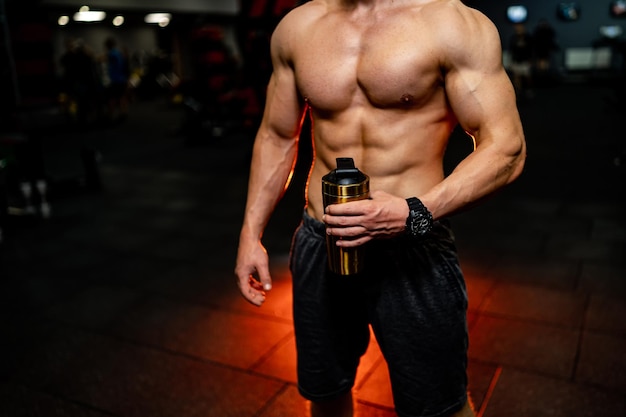 Selective focus of a man with naked torso with protein coctail in bottle in hands. Dark background.
