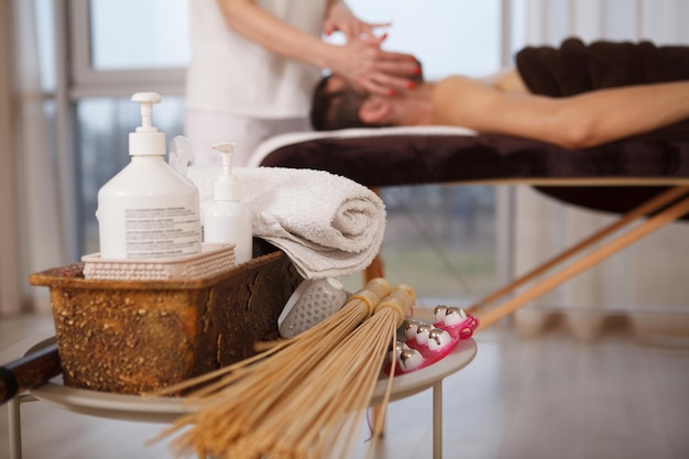 Photo selective focus on massage tools and oils, man getting relaxing massage by spa therapist on background