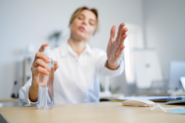 Selective focus of mature businesswoman using antiseptic to disinfect her hands