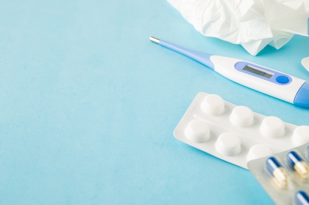 Selective focus on medical pills, used tissue and thermometer on blue background.