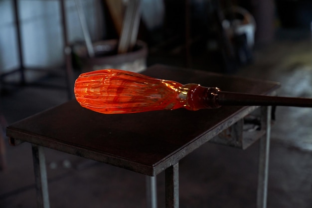 Селективный фокус расплавленного стекла на выдувной трубке на фоне черного стола в темной мастерской