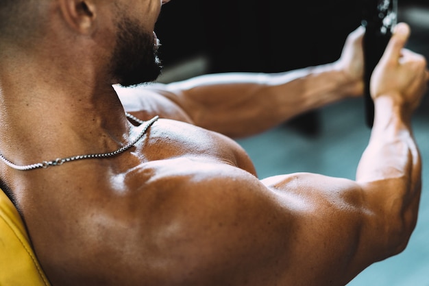 Selective focus on the naked torso of a man exercising with weights in a gym