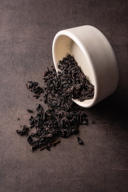 Selective focus, natural black leaf tea. brewing in a clay bowl. vertical angle, macro. on a dark background. for menus and cafes