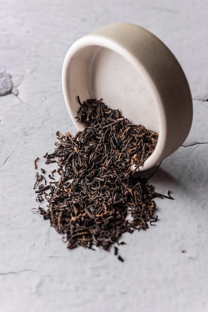 Selective focus natural black leaf tea brewing in a clay bowl vertical angle macro on a light backgr...