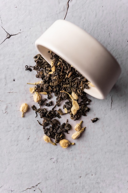 Селективный фокус, натуральный черный листовой чай с цветками жасмина. заваривание в глиняной посуде. вертикальный угол, макро. на светлом фоне. для меню и кафе