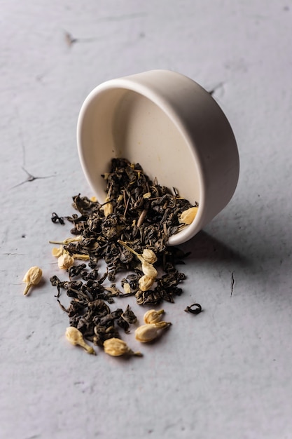 Selective focus, natural black leaf tea with jasmine flowers. brewing in a clay bowl. vertical angle, macro. on a light background. for menus and cafes